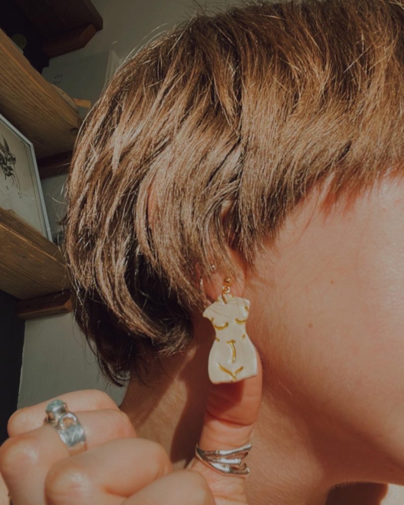 A close up of Grace's profile and earrings that are shaped like a naked body.
