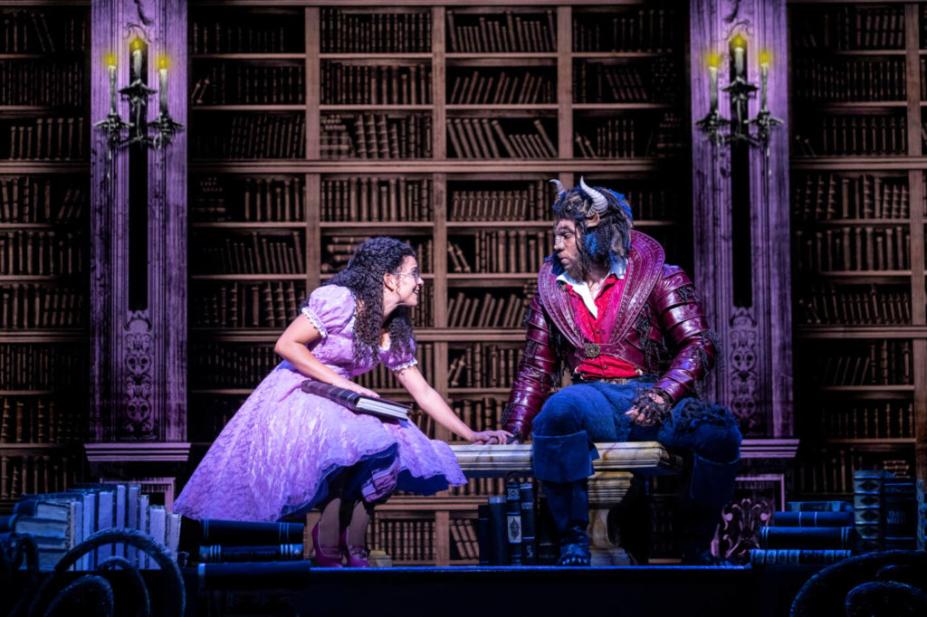 Belle is reading a book to the Beast in the library.