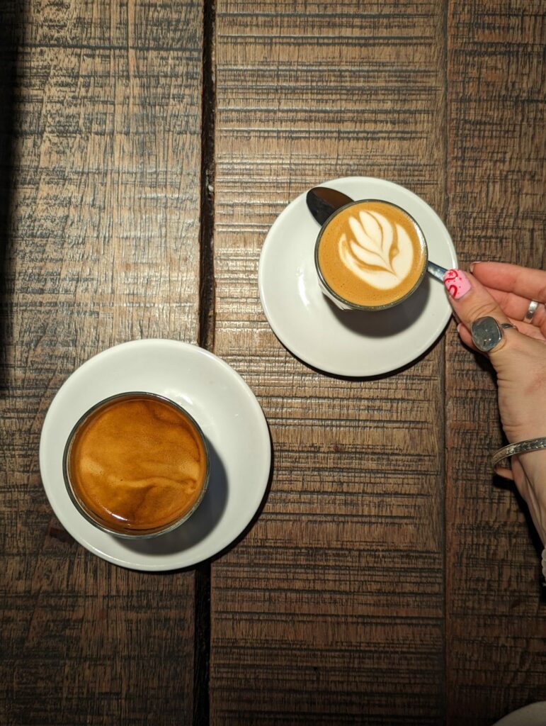 two coffees on a wooden table; a long black with sick crema, and an oat flat white.