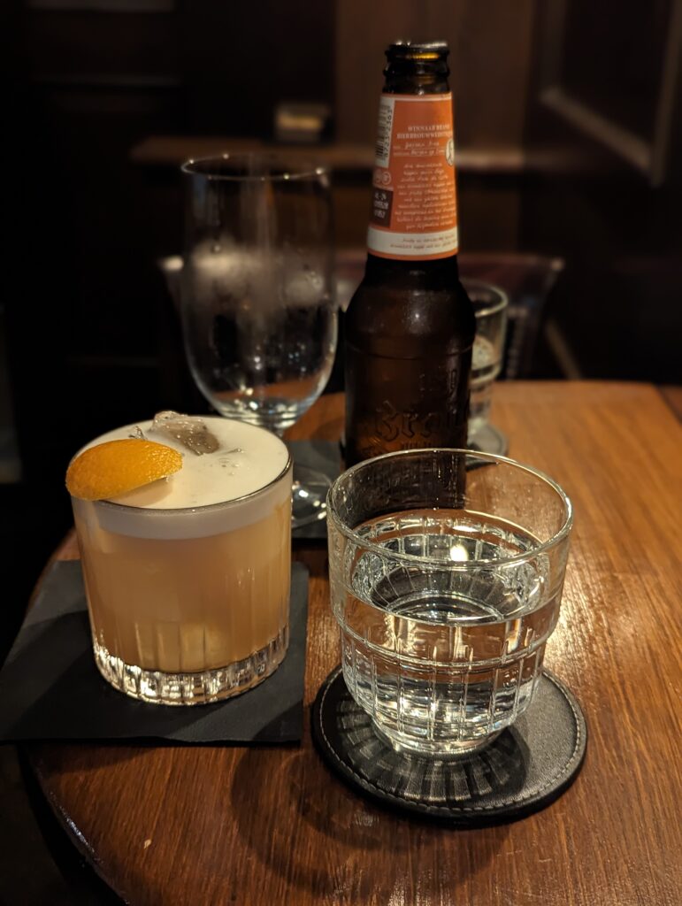 a table at Bar Oldenhof, with a whisky sour (vegan) and beer sitting atop it.